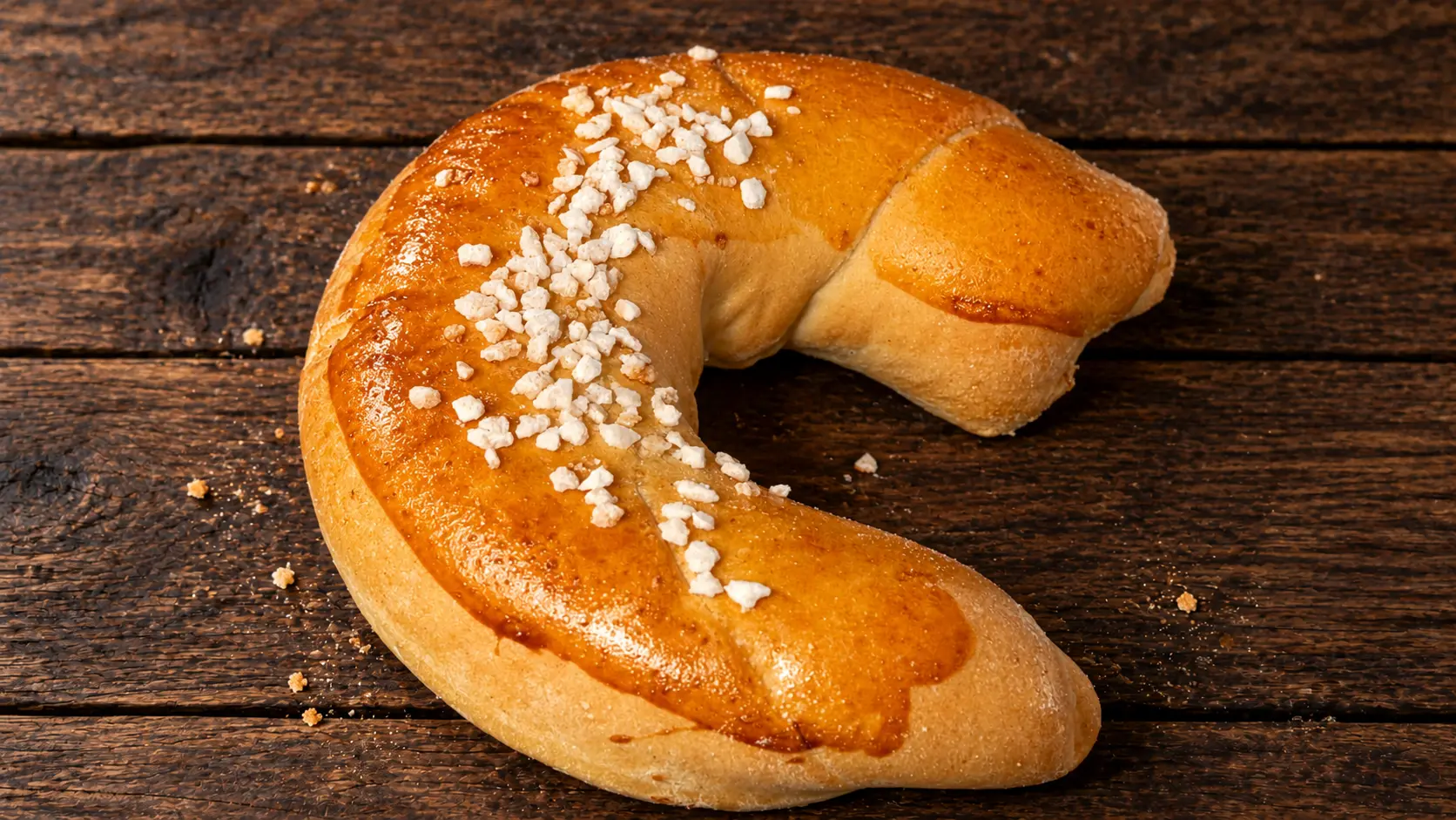Goldbraunes Kipferl mit Hagelsalz auf dunklem Holztisch